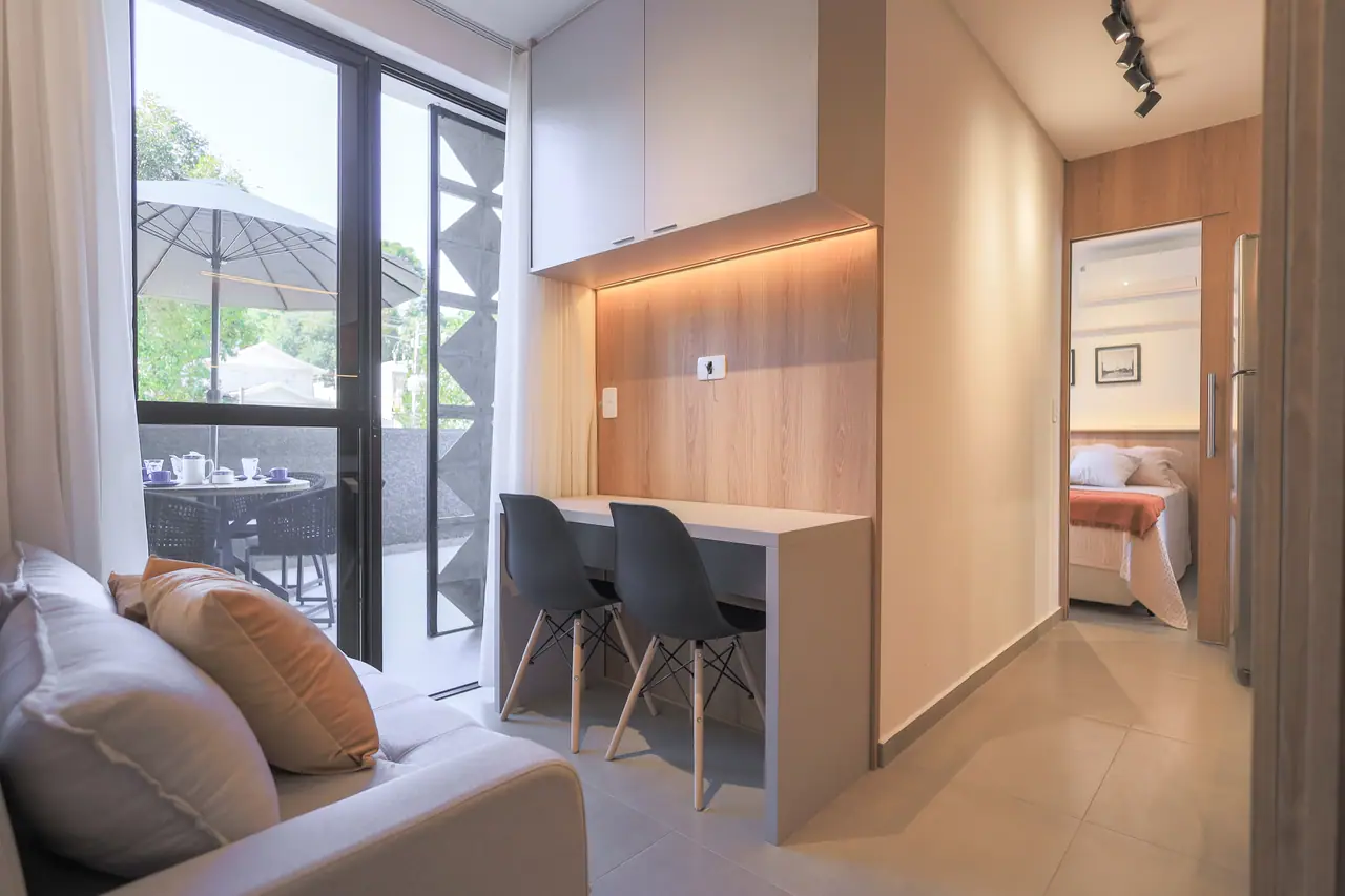 Sala com sofá e bancada, porta de vidro para o terraço e o quarto ao fundo.