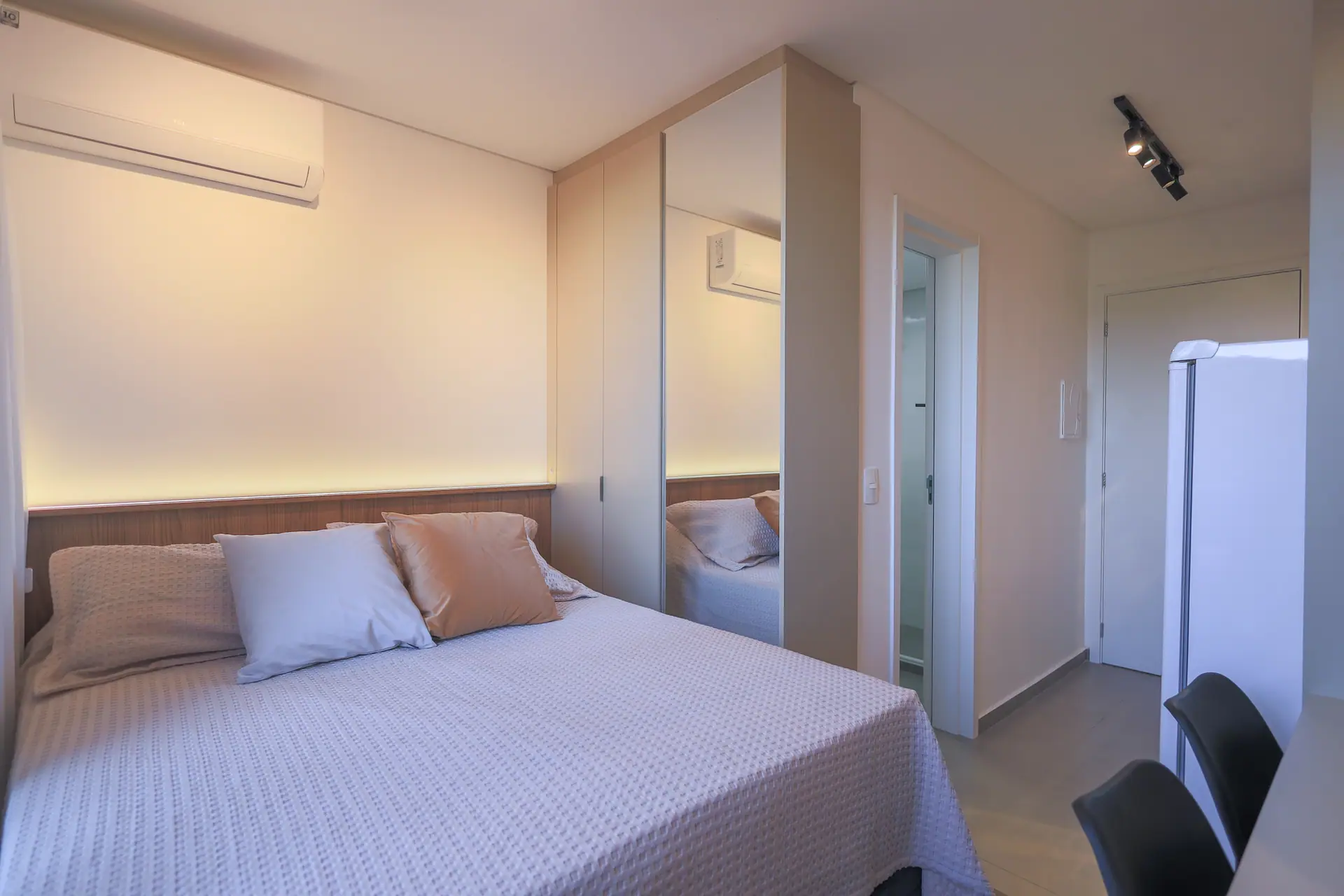Studio inteiro: cama, bancada, armário espelhado e a porta de entrada.